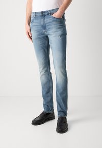 Vaqueros de mezclilla azul claro con acabado desgastado, diseño de pierna recta y bolsillo delantero. Combinados con zapatos náuticos de cuero negro.