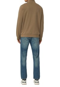 Bruine sweatshirt met een hoge kraag, gecombineerd met lichtblauwe spijkerbroek. De spijkerbroek heeft een klassieke pasvorm met subtiele vervaging en wordt gedragen met witte sneakers.