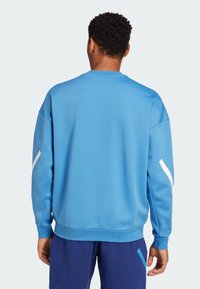 Sinine spordipusa, millel on sile tekstuur, valged diagonaalsed aktsendid varrukatel, ribatud soonikud ja ümmargune kaelus.