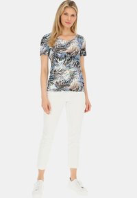 Koszulka z krótkim rękawem, okrągłym dekoltem w niebiesko-beżowy wzór liści, wykonana z elastycznego materiału. Połączona z białymi dopasowanymi spodniami i białymi trampkami.