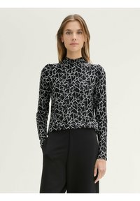 Zwarte top met lange mouwen en een wit hartpatroon, met een hoge, geraffineerde halslijn en een gladde textuur. Gecombineerd met zwarte broeken.