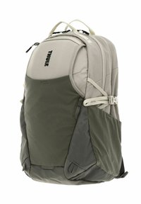 Zaino Thule in beige e verde oliva, con sezioni imbottite, numerosi scomparti con zip e tessuto resistente con finitura strutturata.