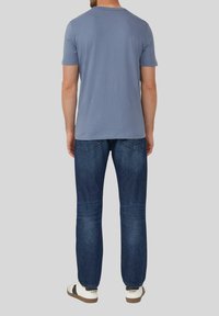 Blauwe katoenen t-shirt voor mannen met korte mouwen, gecombineerd met donkerblauwe spijkerbroek en witte sneakers, gezien vanaf de achterkant.