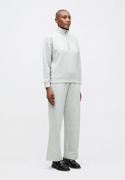 Sivý zipsový sveter s vysokým golierom a zhodné široké nohavice, ktoré majú jemnú textúru a minimalistický dizajn. Čierne topánky dotvárajú celkový vzhľad.