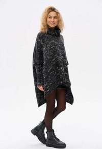 Przestrzenny czarno-biały sweter z mieszanej przędzy z wysokim kołnierzem, rękawami typu batwing i dłuższym tylnym końcem. W połączeniu z czarnymi rajstopami i butami.