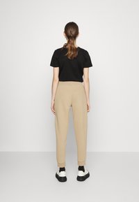 Schwarzes T-Shirt und beiges Jogginghose mit elastischen Bündchen. Die Jogginghose hat eine glatte Textur und das Outfit wird mit schwarzen und weißen Sneakern kombiniert.