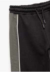 Zwarte joggerbroeken van een gestructureerde zwarte stof met een gladde grijze zijpaneel, voorzien van witte accentstiksels en een elastische tailleband.