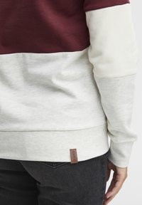 Burgunder, krem og lys grå fargeblokk-sweatshirt med en teksturert bomullsblanding. Har en liten brun logolapp nederst.