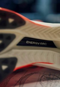 Suola della scarpa con gomma bianca testurizzata e dettagli neri. Marchio visibile "ENERGY ARC" in un accento blu lucido. Rifinitura rossa lungo il bordo.