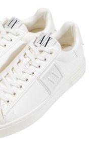 Zapatillas bajas blancas con cordones que presentan logotipos AX en relieve en el lateral y la marca AX impresa en la lengüeta.