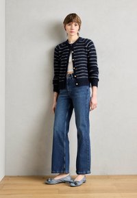 Námořnický pruhovaný cardigan se zlatými knoflíky, spárovaný s džínami s vysokým pasem a šedými balerínami s mašlí.