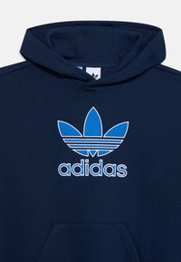 Felpa con cappuccio blu navy con un grande logo Adidas trefoil blu e bianco. Realizzata in morbido tessuto, presenta una tasca a marsupio e polsini a costine.