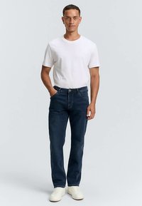 Temno modre jeans hlače z ravnim krojem hlačnic, kombinirane z belo bombažno majico s kratkimi rokavi. Model nosi svetle superge. Enostavna zasnova, brez vzorcev.