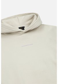 Beige hoodie gemaakt van zacht materiaal, met een trekkoord capuchon, voorlogo in licht paars, en een losse pasvorm.