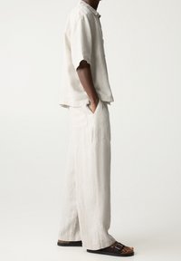 Vaaleanharmaa pellavapaita lyhyillä hihoilla, yhdistettynä leveälahkeisiin housuihin, jotka ovat samasta kankaasta. Ruskeat sandaalit viimeistelevät asun.