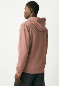 Hooded sweatshirt in dusty rose, made of soft fabric. Long sleeves and a relaxed fit, featuring a kangaroo pocket and ribbed cuffs.