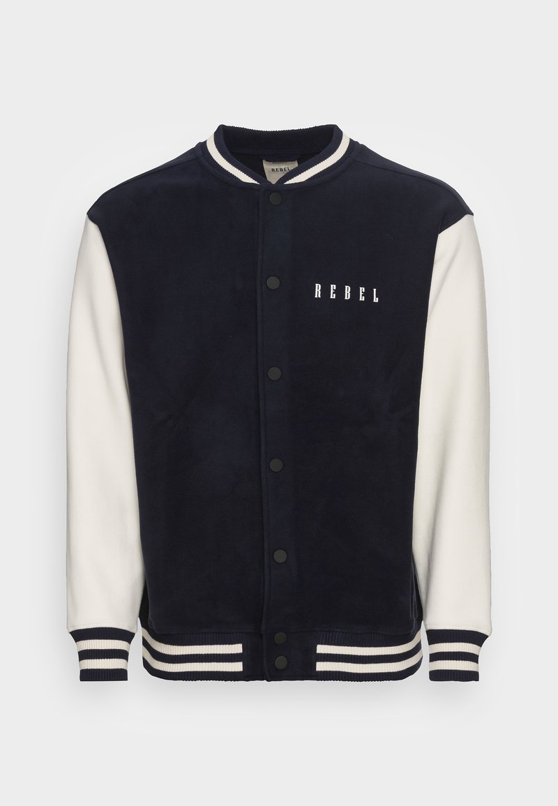 Veste universitaire bleu marine et blanche avec poignets et col rayés, boutons pression à l’avant, et le mot "REBEL" imprimé sur la poitrine gauche.