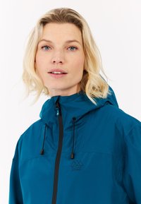 Turkio vandeniui atspari striukė su kapišonu, juodu užtrauktuku ir reguliuojamomis virvutėmis. Ant krūtinės yra logotipas, o medžiaga glotni ir blizgi.