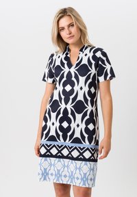 Korte mouw jurk met een marineblauw en witte geometrische print en een V-hals. Het ontwerp bevat gelaagde lichtblauwe accenten aan de zoom.