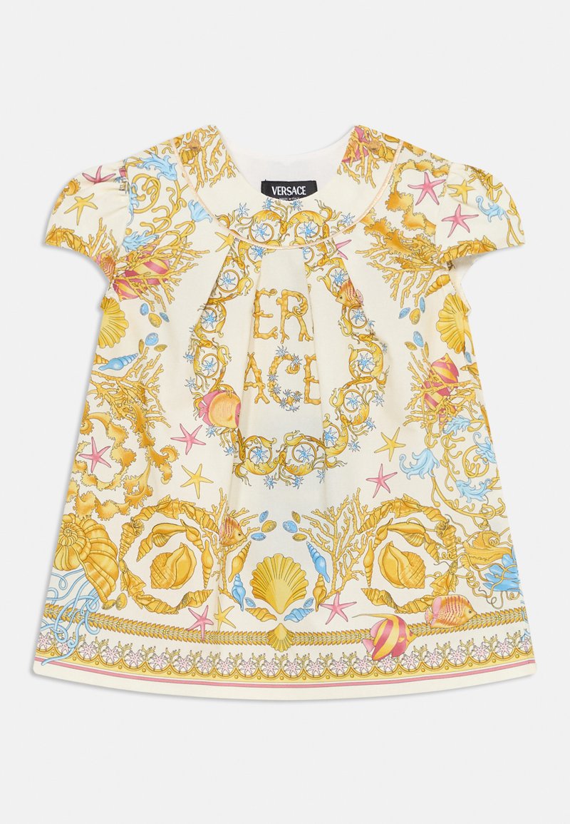 Balta suknelė su ryškiu kriauklių ir koralų raštu, papuošta auksiniais akcentais. Trumpi pūsti rankovės ir susiraukšlėjimai prie iškirptės.