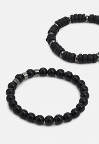 To svarte armbånd: det ene med glatte, runde perler og metalliske detaljer, det andre med teksturerte, sylindriske perler. Begge har en ensartet form.