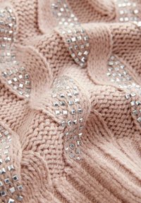 Gestrickter Pullover in sanftem Rosa mit erhobenem Kabelmuster, verziert mit silbernen quadratischen Nieten, die in horizontalen Linien angeordnet sind.