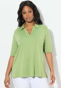Grön polo med korta ärmar, v-ringad krage, sidosplashar och en mjuk textur, designad för en avslappnad passform.