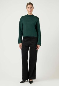 Zielony krótki sweter z wysokim kołnierzem, długimi rękawami i subtelny połysk, w połączeniu z czarnymi spodniami o wysokim stanie i szerokich nogawkach. Czarnym, szpiczastym obuwiem.