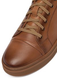 Zapatilla alta de cuero marrón con cordones planos, puntera redondeada, suela de goma texturizada y costuras en la parte superior.