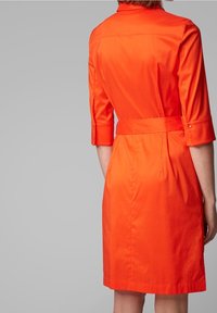Pomarańczowa bawełniana sukienka z dopasowanym talią, rękawami trzy czwarte i paskiem do związania. Gładka tekstura, prosta konstrukcja i subtelne szwy z tyłu.