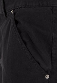 Gros plan d'une poche de jean en denim noir avec coutures visibles et rivets en métal.