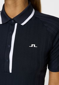 Polo shirt blu navy con un design a righe testurizzato, colletto bianco e bottoni. Presenta un piccolo logo bianco sul lato sinistro.