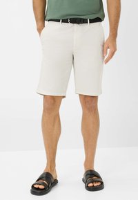 Shorts beige con taglio dritto, due tasche laterali e orlo arrotolato; abbinati a sandali neri scivolati e una cintura intrecciata nera.