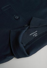 Nära bild av en mörk marinblå knappad ärmslut med synlig etikett på insidan som säger "THE SET MADE IN BANGLADESH."