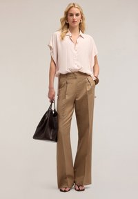 Blusa rosa chiaro a maniche corte con bottoni; pantaloni beige a vita alta, sartoriali; borsa a tracolla in pelle nera; sandali neri; stile minimalista.