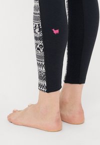 Black leggings featuring a patterned side panel in white and gray with geometric designs, and a small pink embroidered logo on the left leg.