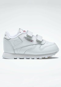 Hvit lær sneakers med borrelåsremmer, polstret krage og teksturert gummisåle. Har Reebok-logo i sølv.