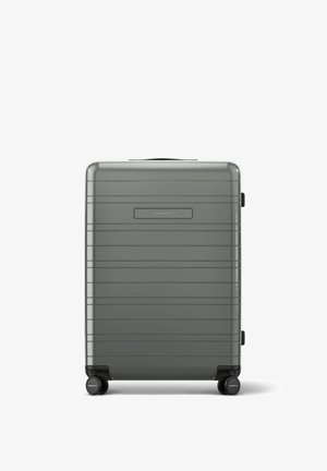 Valise rigide grise avec des rainures, une poignée supérieure et quatre roulettes. Elle dispose d'un petit espace pour une étiquette d'identification et d'une finition lisse et brillante.