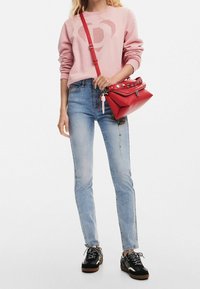 Vaaleanpunainen huppari sydänkuviolla, vaaleansiniset kapeat farkut, punainen olkalaukku niiteillä ja mustat liikuntakengät valkoisilla yksityiskohdilla.