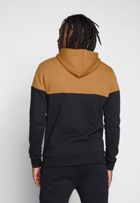 Felpa con cappuccio dal design color block; sezione superiore color cammello e sezione inferiore nera. Tessuto morbido, polsini e orlo a costine.