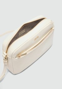 Cremfarbene Leder-Crossbody-Tasche mit Reißverschluss, goldfarbener Hardware und gefüttertem Innenfutter mit Muster. Kompakte rechteckige Form.