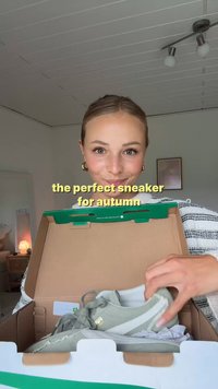 Lys grå sneakers med teksturert overflate, hvite detaljer og grå snøringer. Eske med grønn lokk åpen, som viser sneakersen inni.