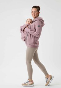 Felpa rosa con zip e tasca per bambini, abbinata a leggings beige e sneakers multicolori. Presenta un logo sul manica.