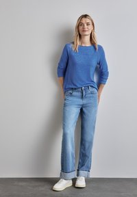 Haut à manches longues bleu avec un col rond, associé à un jean large bleu clair et des baskets blanches. Design simple et décontracté avec des poignets retroussés.