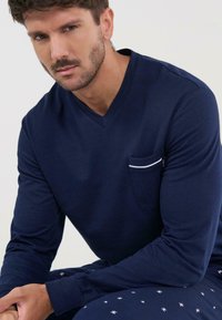 Top azul marino de manga larga con escote en V y bolsillo, con un acabado en blanco; combinado con pantalones de pijama con un patrón que presenta pequeños motivos de estrellas.