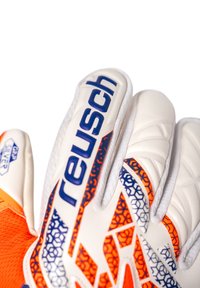 Guanti da portiere bianchi e arancioni con superficie di presa testurizzata, motivi esagonali e marchio "reusch" in blu sulle dita.