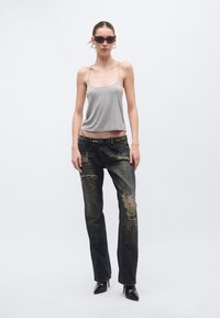 Hall hall top, millel on õhukesed traksid, kombineeritud kulunud tumedate teksapükstega, mis on kaunistatud hõbedaste naelte ja rebenditega, täiendatud mustade teravate kontsadega.