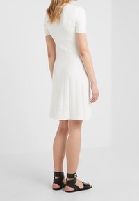 Robe blanche côtelée avec un ourlet évasé, des manches courtes et un corsage ajusté, assortie à des sandales noires à lanières et des brides à la cheville.