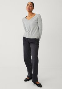 Lys grå, langærmet v-hals sweater med sideskår ved kanten, parret med mørke grå jeans og sorte flade sko. Glat tekstur, afslappet pasform.