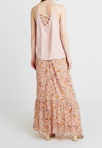 Světle růžový top na ramínka s překříženými zády v kombinaci s květinovou maxi sukňou v odstínech broskve a oranžové, se zvýšeným designem.